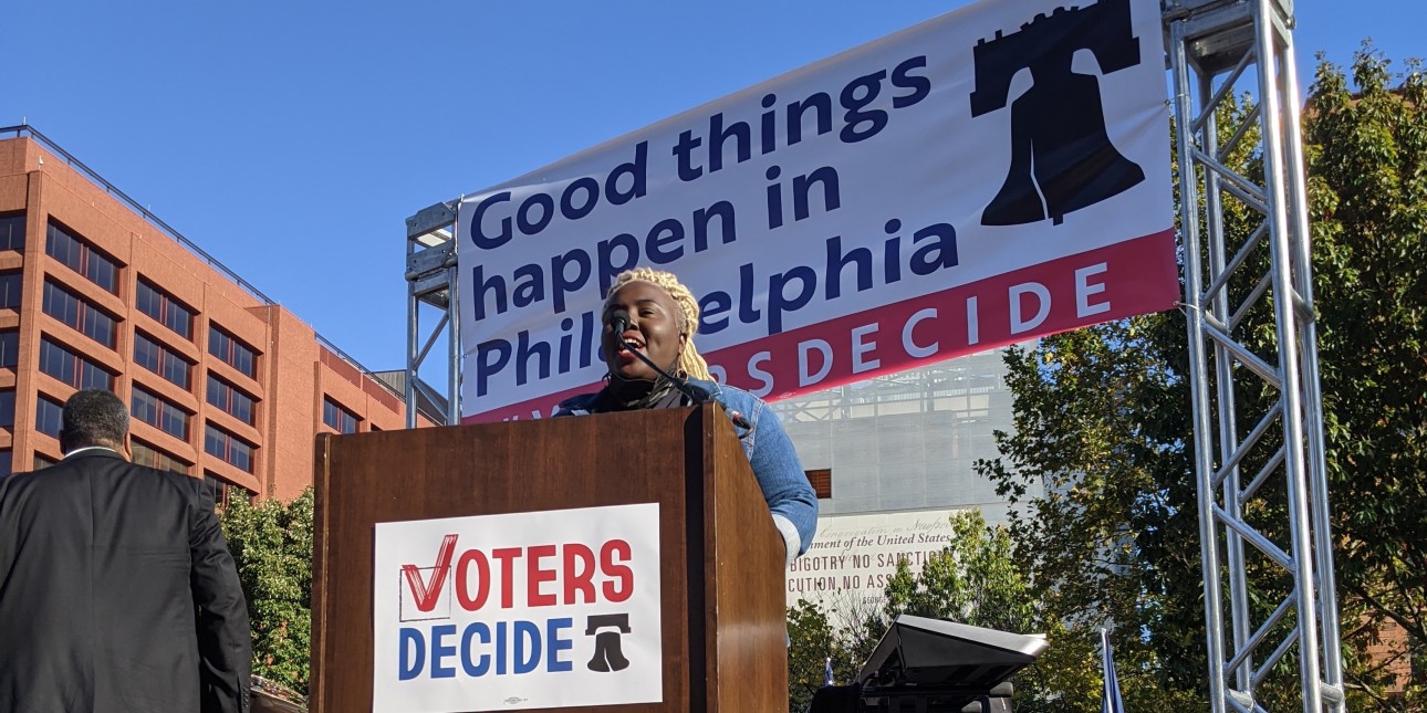 Nikki Grant speaks at a podium with a 'Voters Decide' sign on it and a 'Good things happen in Philadelphia sign behind it